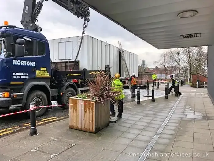 Nortons hiab placing a large white unit under a building canopy on a city street
