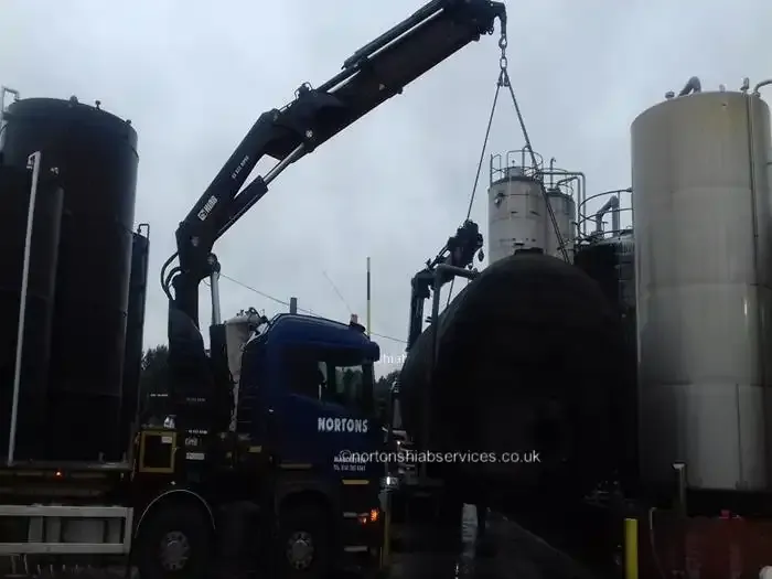 Nortons eight-wheel rigid hiab lifting a large black process vessel between silos