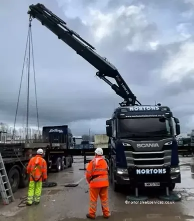 Nortons Scania 858 with the crane up and two men in orange overalls beside it on a wet yard