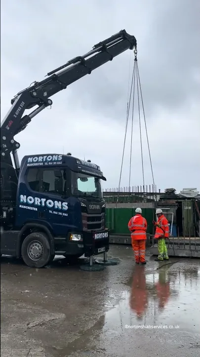 Nortons Scania 858 with the crane up and chains hanging, two men in orange on a wet yard