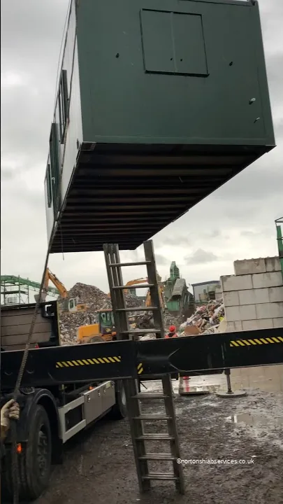 Green anti vandal cabin held on the crane above a Nortons trailer on a demolition site