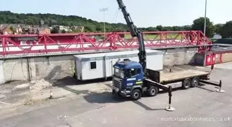 Long white anti vandal cabin on the deck of a Nortons trailer in front of a red stand