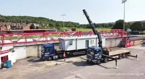 Nortons hiab lifting a white portable cabin at a sports ground