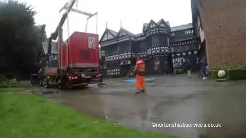 Red travelling arts unit set down on hardstanding in front of a black and white timbered hall, with a banksman in orange