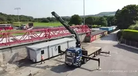 Nortons 855 hiab lifting a cabin with a stand and hills behind
