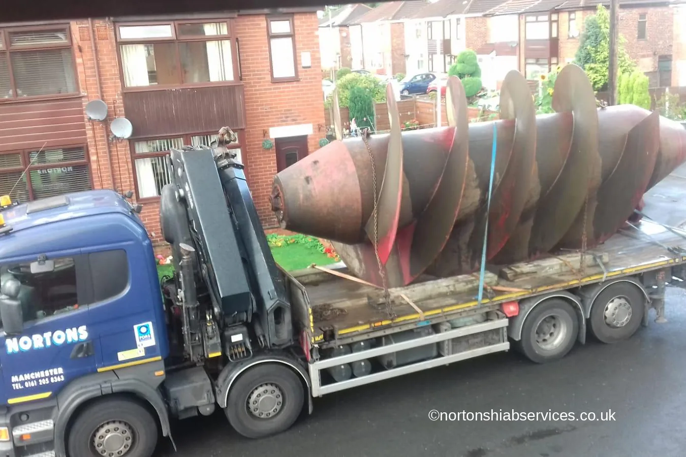 A Nortons hiab lorry carrying an Archimedes screw chained to its deck through a residential street