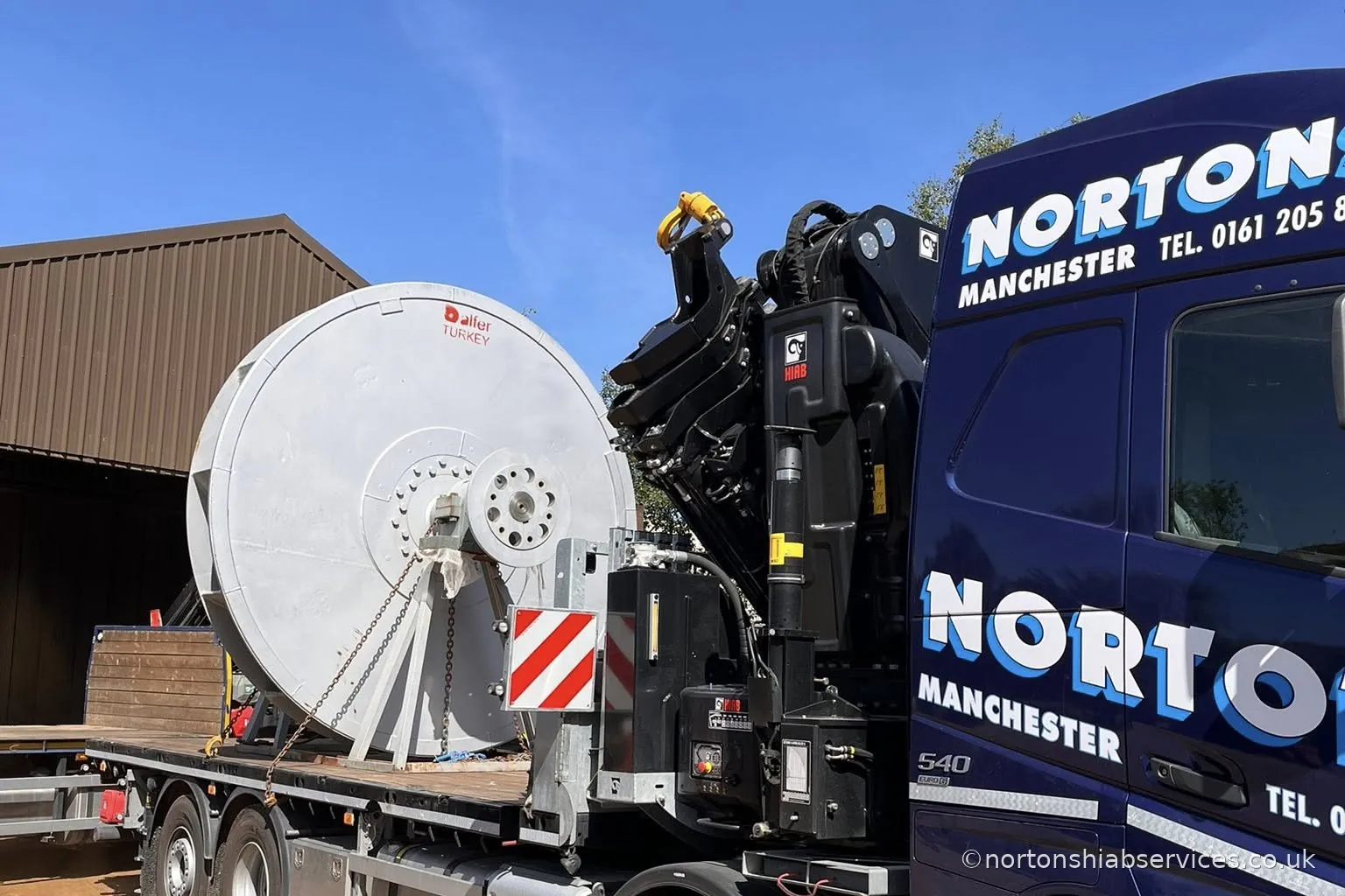 A very large steel drum loaded on a Nortons Volvo rigid with a wide load marker board fitted