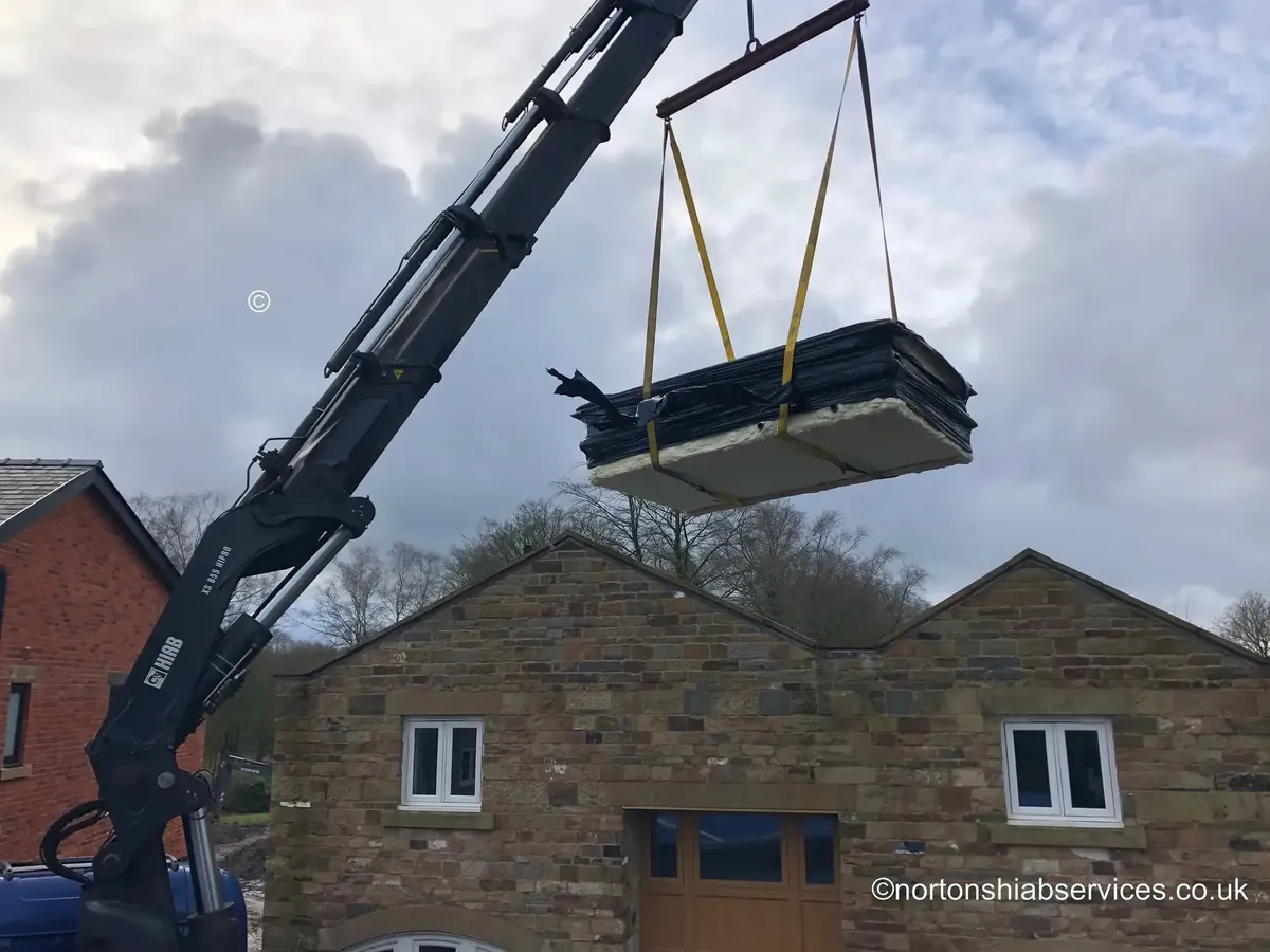 A Nortons hiab holding a large wrapped panel level in the air beside a stone outbuilding, carried in from the road